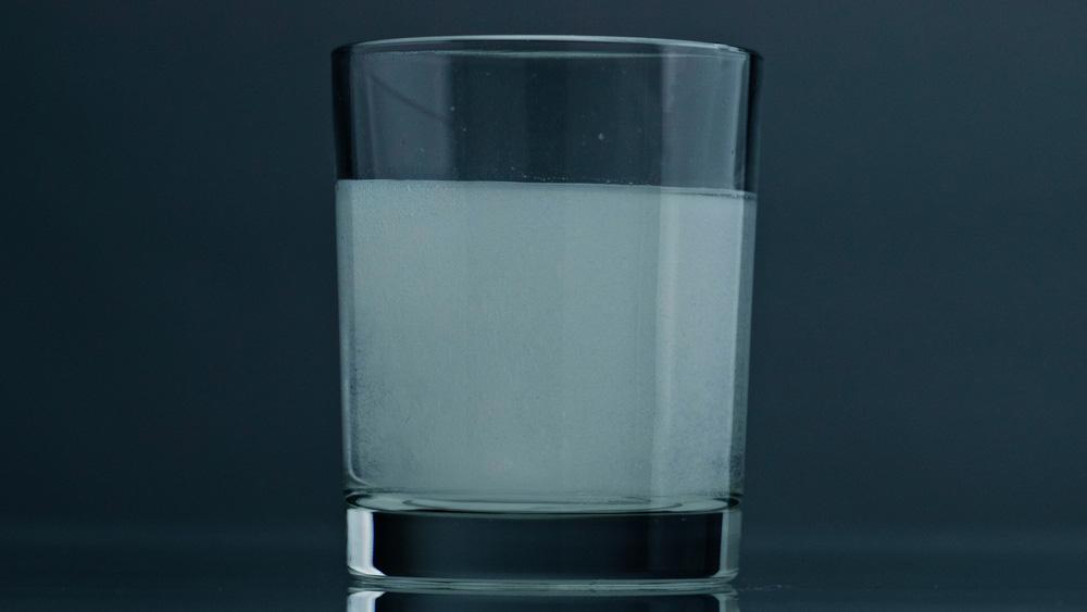 Glass of cloudy milky white water indicating bacterial contamination or turbidity — a sign of coliform or iron bacteria in a Southeast Texas well water supply treated by Clear Solution Services